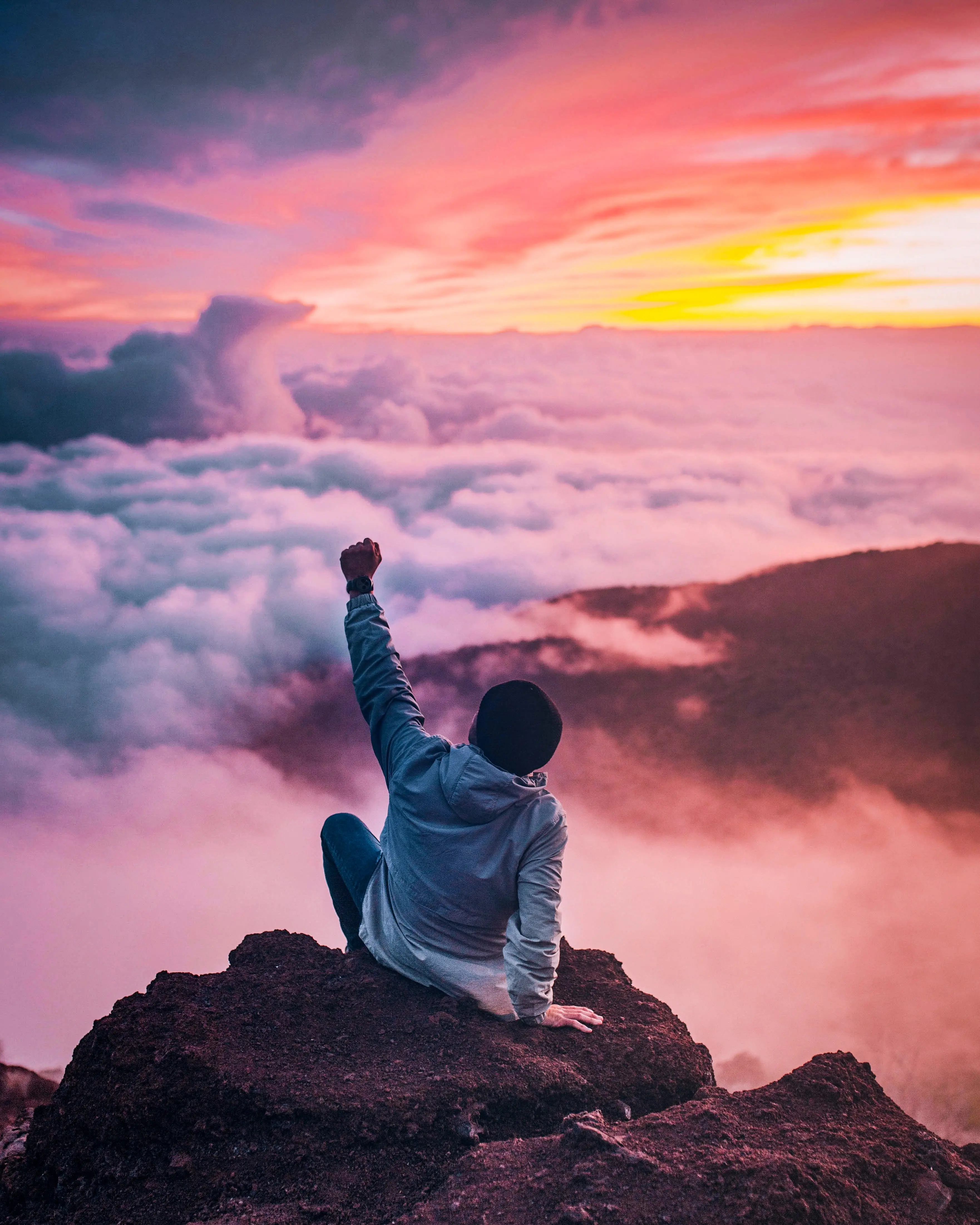 a man sitting on a mountain and rising the fist because he had achived everything in his life